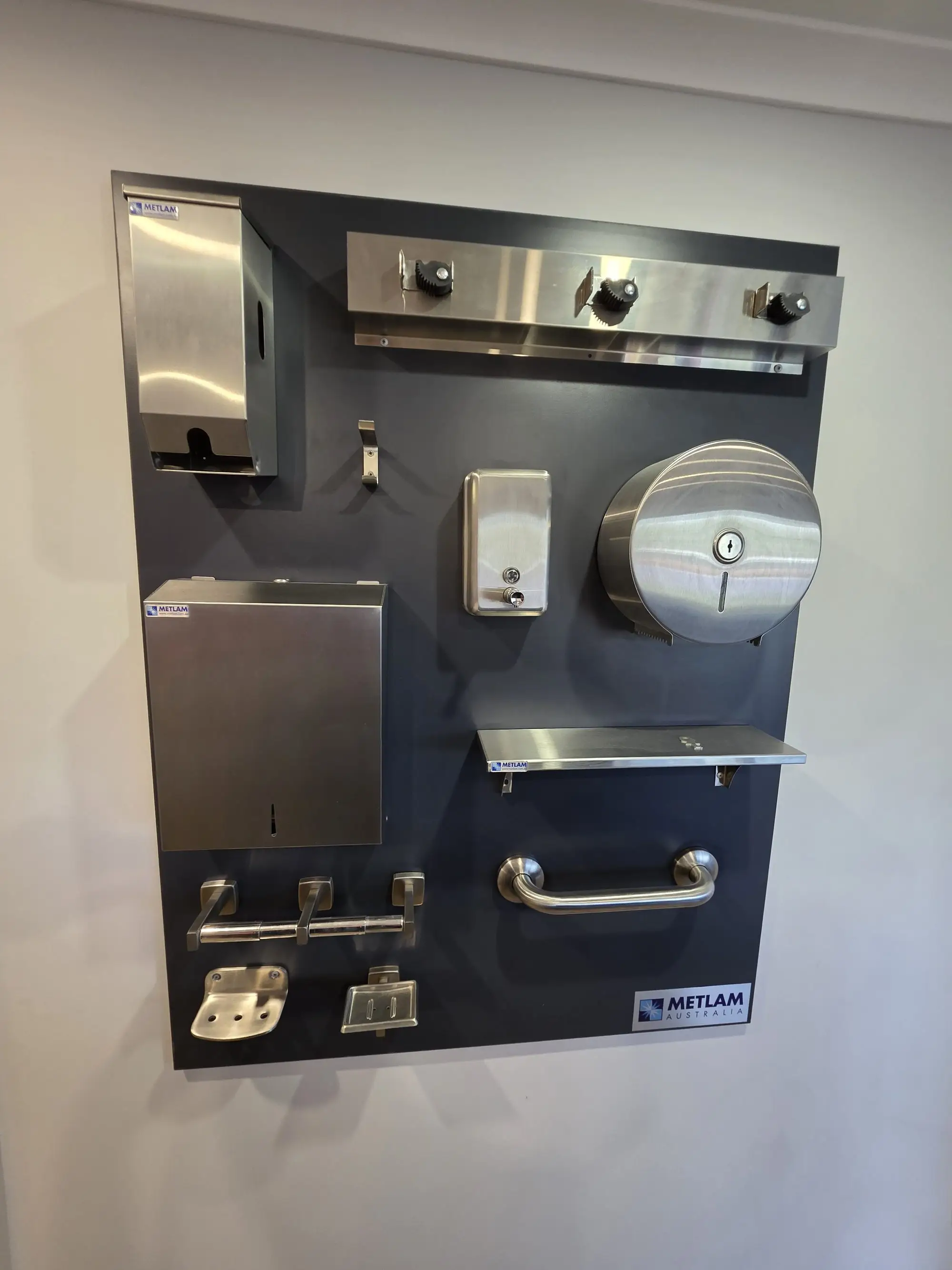 A Metlam washroom board with stainless dispensers, a grab rail and a shelf.